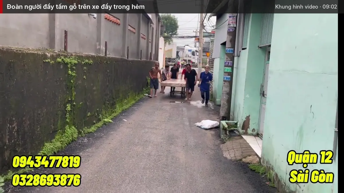 Đoàn người đẩy tấm gỗ trên xe đẩy trong hẻm